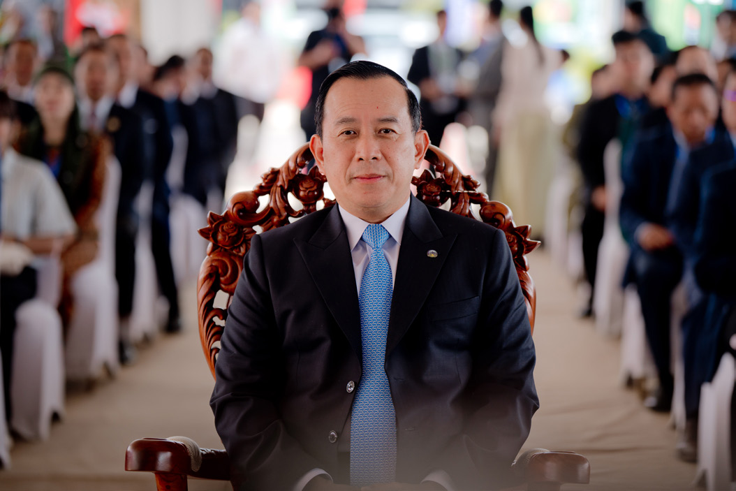 A dignitary seated in a carved wooden chair at a formal ceremony.
