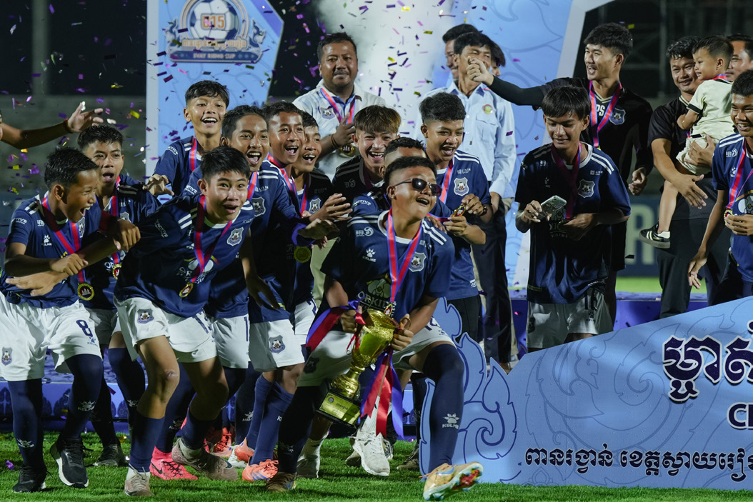A youth football team celebrating with the trophy under falling confetti.