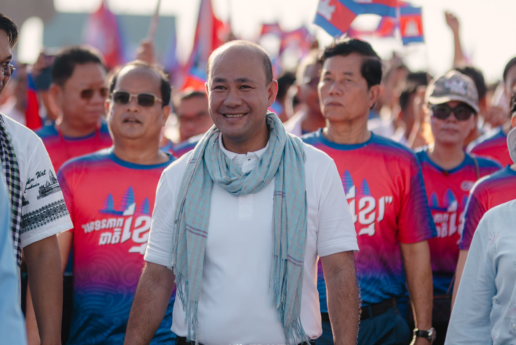 A man in a white shirt and krama walking through a crowd of supporters.