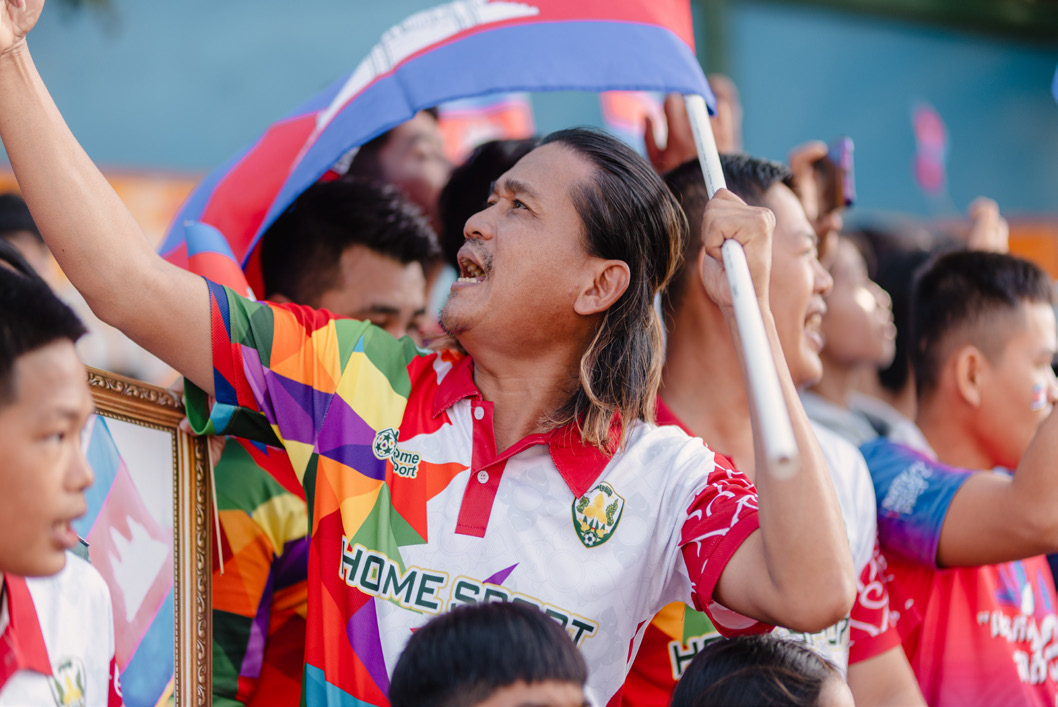 Supporters cheering in the stands beneath a Cambodian flag.